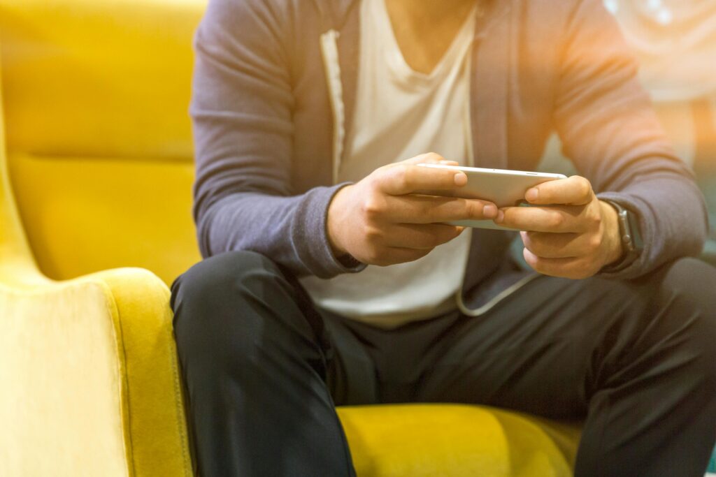 A man sits on a yellow chair using a smartphone, showcasing technology use.